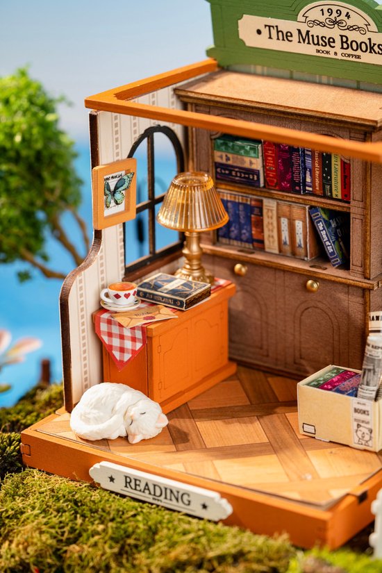 Miniatuur boekenwinkel interieur met boekenplanken, lamp, kopje thee en slapende kat.