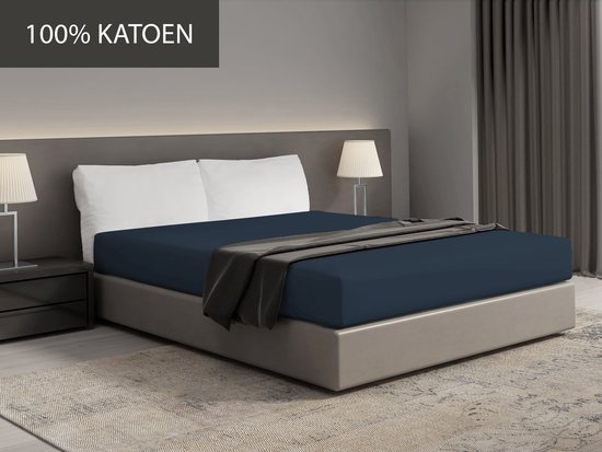 Drap-housse bleu foncé sur un lit avec le texte '100% COTON'.
