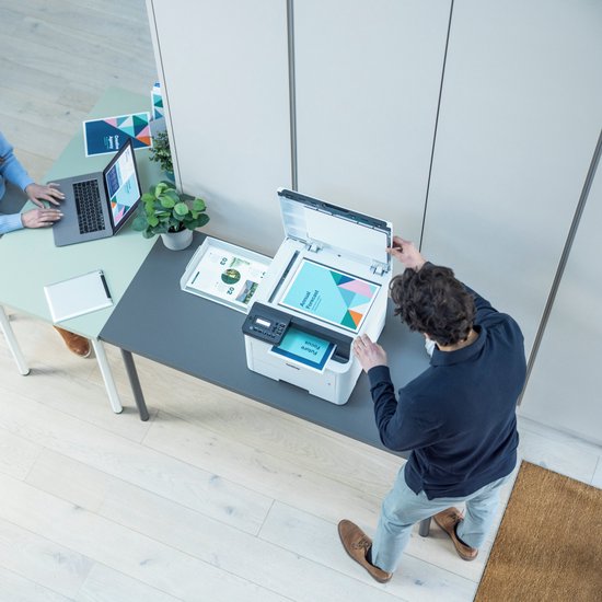 Twee personen gebruiken een witte Brother printer in een kantooromgeving.