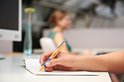 Hand die met een oranje STABILO pointball balpen met blauwe grip in een notitieboekje schrijft.