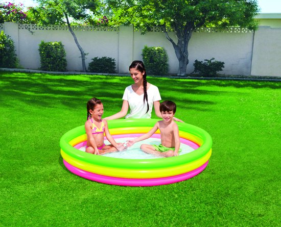 Een vrouw en twee kinderen genieten van een driekleurig opblaasbaar zwembad in een weelderige groene tuin.