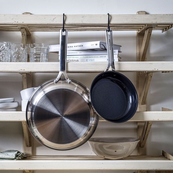 Twee koekenpannen hangen aan haken. Een met zilverkleurige buitenkant, de andere met zwarte antiaanbaklaag.