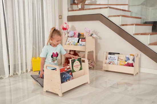 Houten kinderboekenkast met een meisje dat naar de boeken kijkt. Een geel speelgoedblok staat naast de kast.