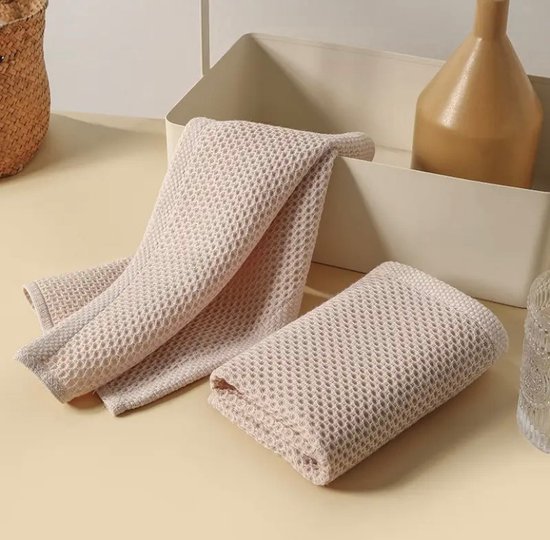 Twee beige handdoeken met honingraatpatroon op een tafel, één gevouwen, één open.
