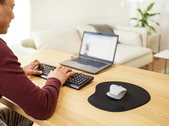 Tapis de souris noir avec repose-poignet, avec une souris dessus, sur un bureau en bois, pendant qu'un homme travaille sur un ordinateur portable.