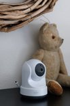 Witte babyfoon camera naast een teddybeer onder een krans.