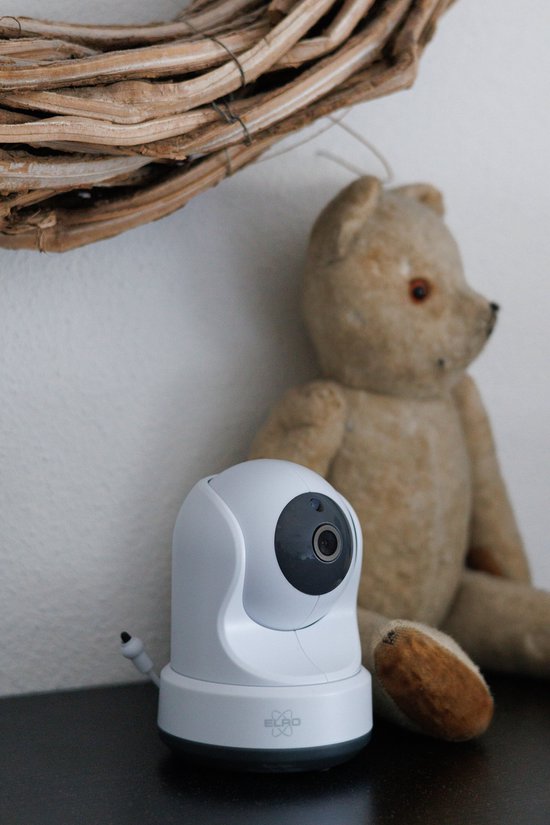 Witte babyfoon camera naast een teddybeer onder een krans.