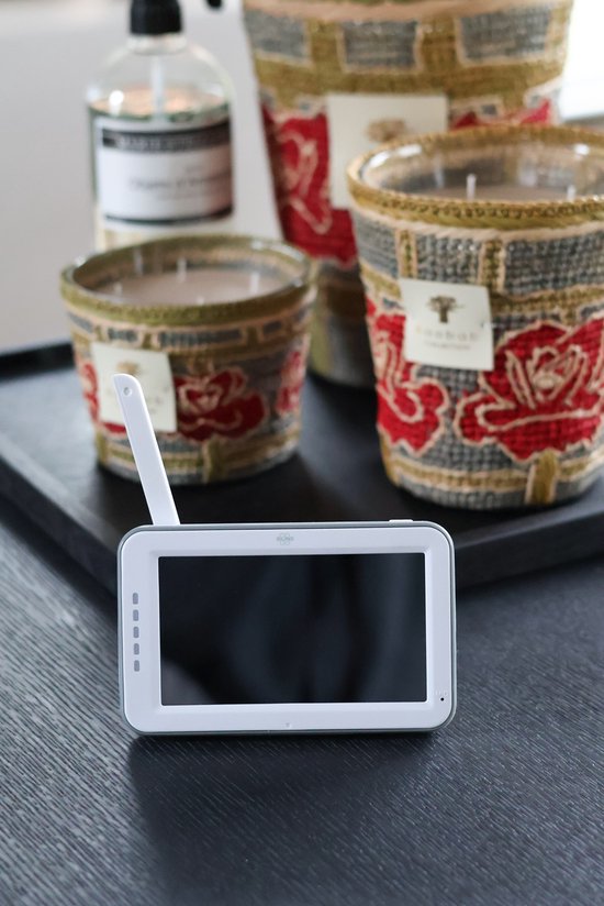 Witte babyfoon monitor met antenne op een donkere tafel, met decoratieve potten op de achtergrond.