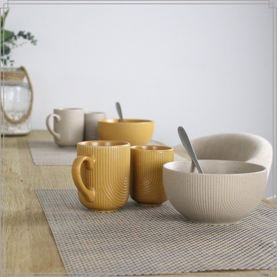 Mise en place de table avec des tasses et un bol jaunes, et des tasses et un bol blanc cassé à motif côtelé.