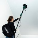 Vrouw met rugzak schuurt een hoog plafond met een lange groene schuurmachine.