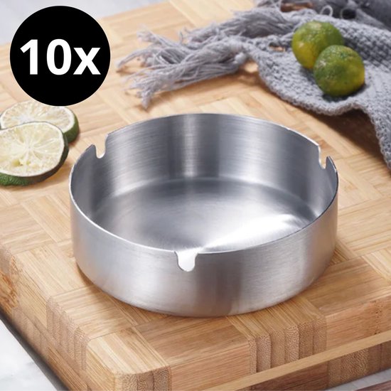 Ronde, metalen asbak met inkepingen voor sigaretten, op een houten ondergrond met limoenen en een grijze sjaal.