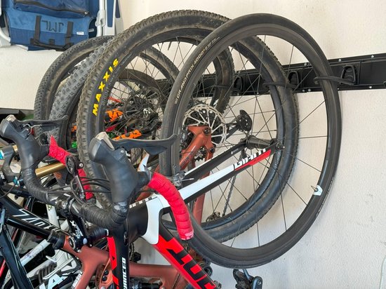 Twee racefietsen met rode accenten hangen aan een zwarte muurbeugel.