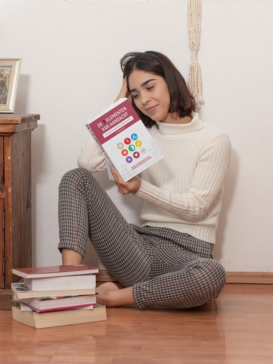 Vrouw in witte coltrui en geruite broek zit op de grond, leest boek 'De 7 elementen van aandacht'.