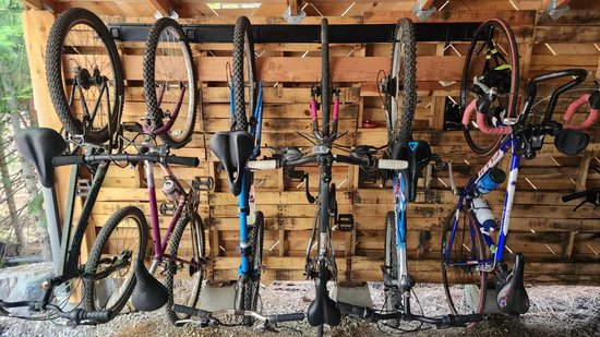 Houten schuur met aan de muur 6 fietsen, waarvan 2 mountainbikes, opgehangen aan zwarte haken.