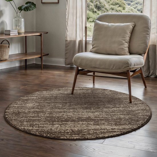 Rond bruin vloerkleed met verweerd, gestreept patroon onder een stoel in woonkamer.