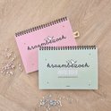 Twee kraambezoek invulboeken, één roze en één groen, op een houten ondergrond.