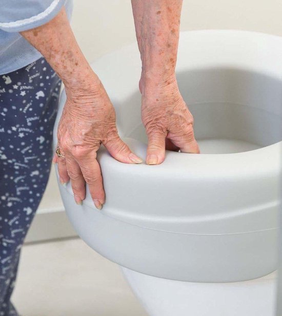 Grijze handen van een persoon met een bril met gouden rand op een witte toiletverhoger.
