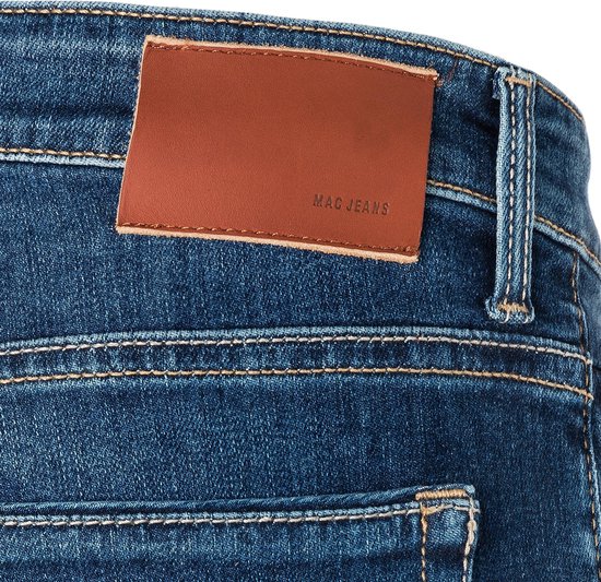 Detail van de achterkant van een blauwe jeans met een bruin lederen MAC JEANS label.