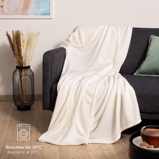 Witte fleece deken gedrapeerd over een donkere bank, met wasinstructies.