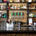 Bar met flessen op de achtergrond en een drankdispenser met gekleurde dranken.