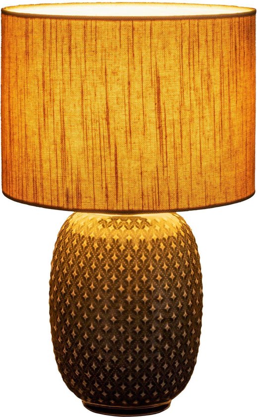 Grijze tafellamp met beige stoffen kap en decoratieve voet, verlicht.