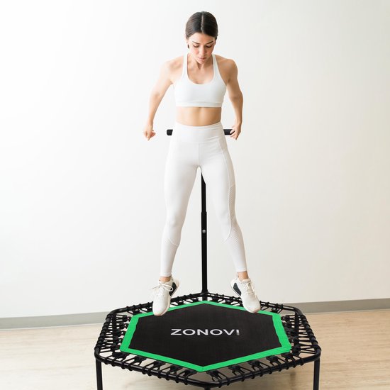Een vrouw in sportkleding springt op een zwart-groene trampoline met handvat.