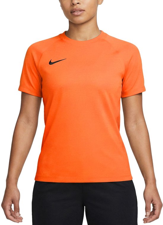 Model draagt een oranje sportshirt van Nike met korte mouwen en zwarte broek.