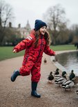 Meisje in rood regenpak met donkerblauwe bloemenprint, lopend naar eenden bij een waterplas.