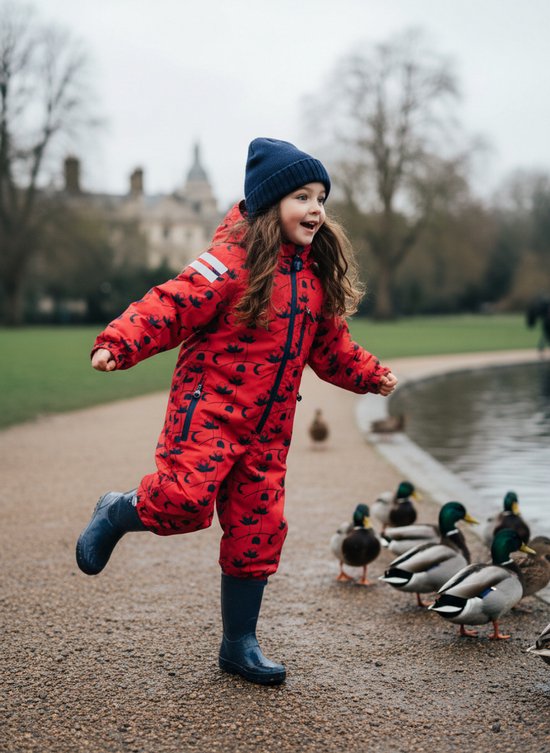 Meisje in rood regenpak met donkerblauwe bloemenprint, lopend naar eenden bij een waterplas.