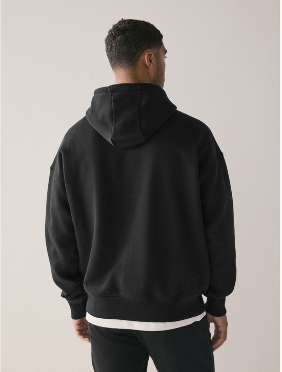 Man met de rug naar de camera, draagt een zwarte oversized hoodie met capuchon.