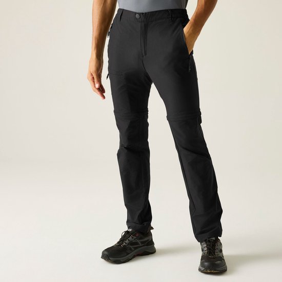 Man met donkere huid, gekleed in een grijze polo en zwarte afritsbare broek.