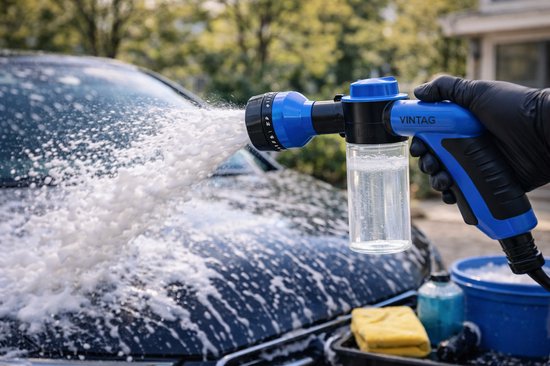 Hand met zwarte handschoen houdt blauwe Vintag schuimsproeier vast, spuit schuim op auto.