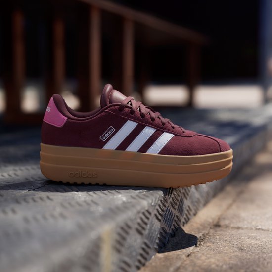 Bordeauxrode Adidas sneakers met witte strepen, dikke bruine zool en roze hiel.