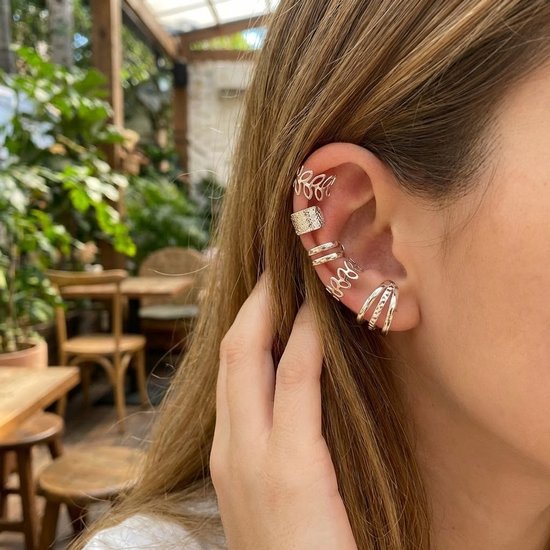 Oor van een model met meerdere gouden oorclips: een blad-, een geribbelde- en een bandjesdesign.