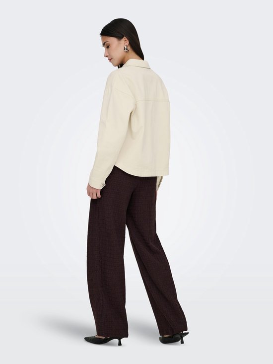 Model draagt een gebroken witte spijkerjas met lange mouwen en donkerbruine broek, met een zwarte tas over de schouder.