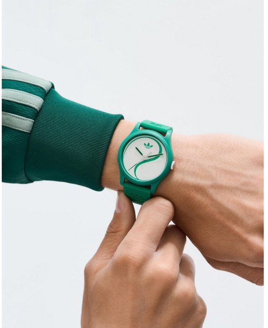 Groen siliconen Adidas horloge met witte wijzerplaat met yin-yang-achtig groen patroon, gedragen om een pols.