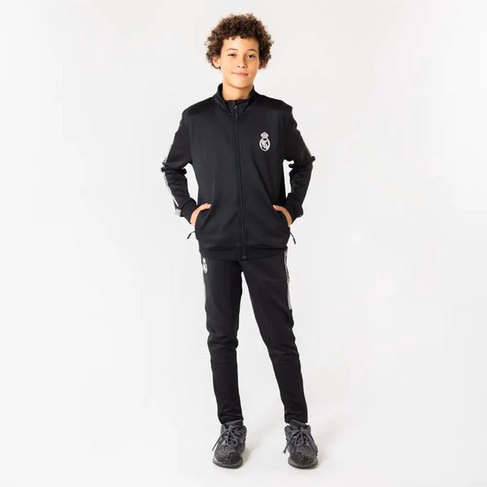 Jongen in zwart trainingspak van Real Madrid. Vest met Real Madrid logo en broek met Real Madrid strepen op de zijkant.
