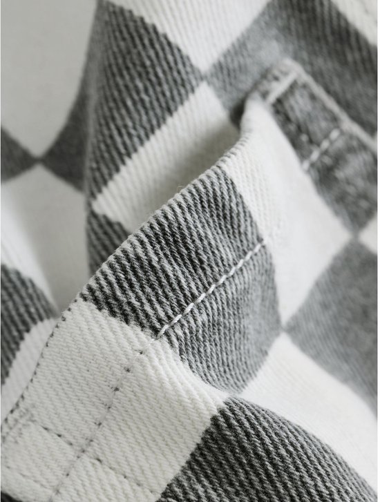 Close-up van de textuur en de gestikte naden van de grijs-witte geruite stof.