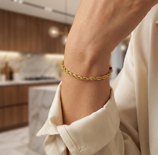 Bracelet torsadé doré porté au poignet d'une femme, avec une blouse en soie crème.