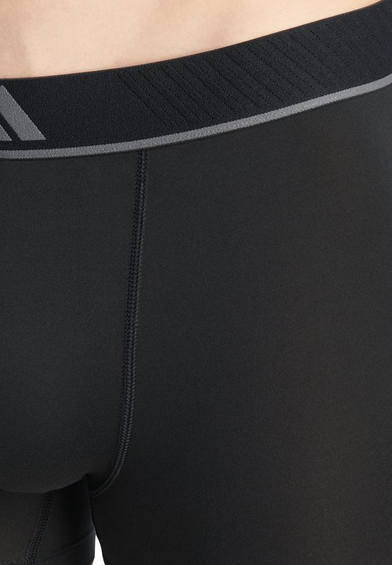 Close-up van de grijze, gestreepte tailleband van zwarte Adidas boxershorts.