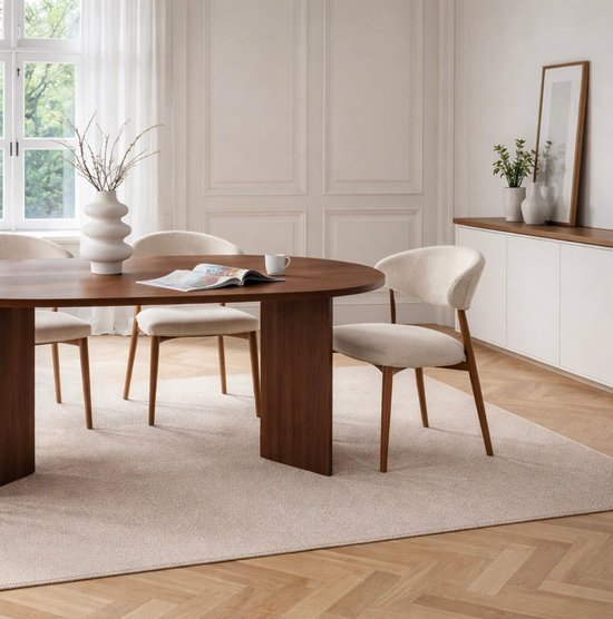 Ovale eettafel van donker hout met drie beige stoffen stoelen met houten frame.