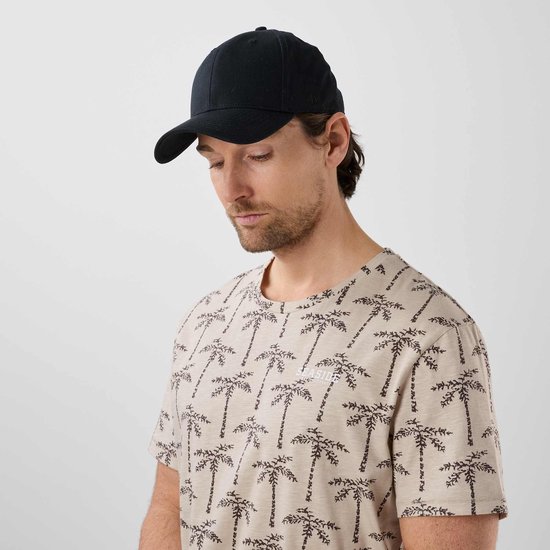 Man met beige T-shirt met palmbomenprint en zwarte pet.
