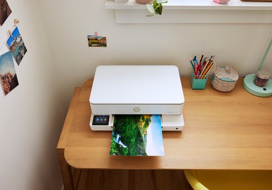 Witte HP Envy printer print een landschapsfoto op een houten bureau.