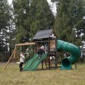 Kinderen spelen op een groen speeltoestel met dubbele glijbaan en buisglijbaan.