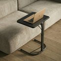 Zwarte laptoptafel met een laptop erop, naast een beige bank.
