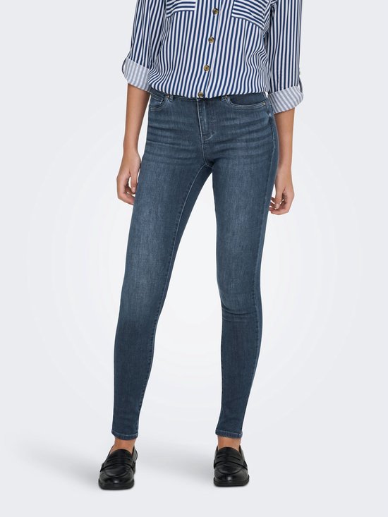 Model in donkerblauwe skinny jeans, gezien van voren. Gestreepte blouse met opgerolde mouwen en zwarte loafers.