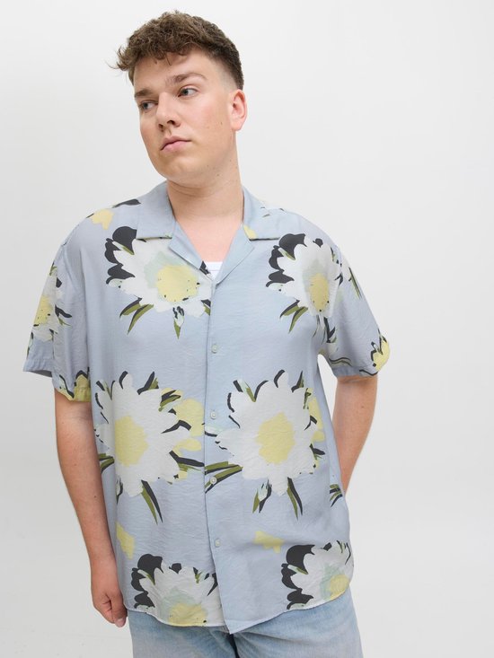 Man met handen in zakken, draagt lichtblauw kort hemd met bloemenprint.