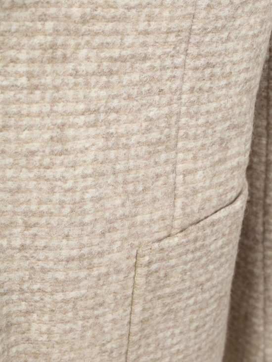 Detail van beige colbertstof met klein ruitjespatroon en een opgestikte zak.
