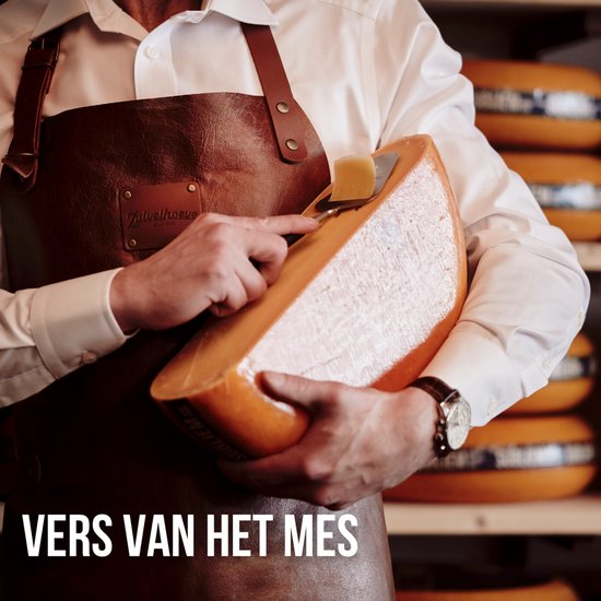 Een man in een schort schaaft kaas van een groot rond stuk kaas.