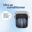 Compacte, witte mini-airconditioner met zwarte voorkant. Blaast blauwe luchtstroom. "Mini air conditioner"